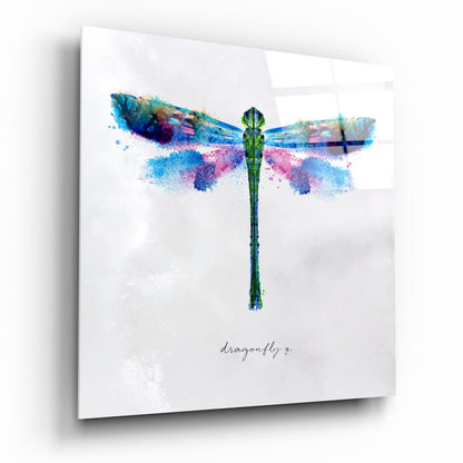 Watercolor dragonfly glass wall art with vibrant blue, pink, and green splattered wings and green body on white background, with "dragonfly" text below.