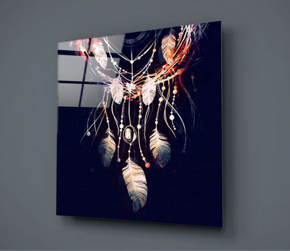 Glass wall art panel displaying an ornate dreamcatcher with feathers, beads, and chains on dark background, mounted at angle against gray wall.