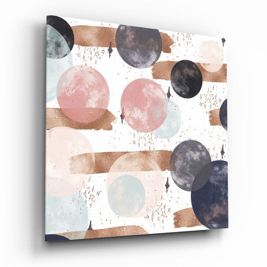 Angled view of square glass wall art featuring watercolor moons in pink, black, and blue with bronze brushstrokes and gold speckles on white background.