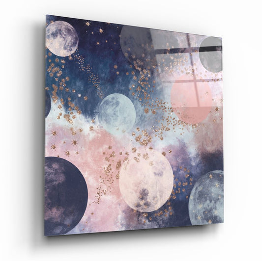Glass wall art panel displayed at an angle showing moons, stars, and gold particles against navy and pink watercolor backgrounds.