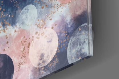 Close-up angled view of glass wall art displaying moons in pink and blue tones with gold sparkle accents.