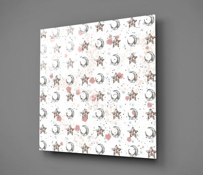Square glass wall art panel displayed at an angle showing repeating pattern of bronze stars, crescent moons, and pink watercolor splashes on white background.