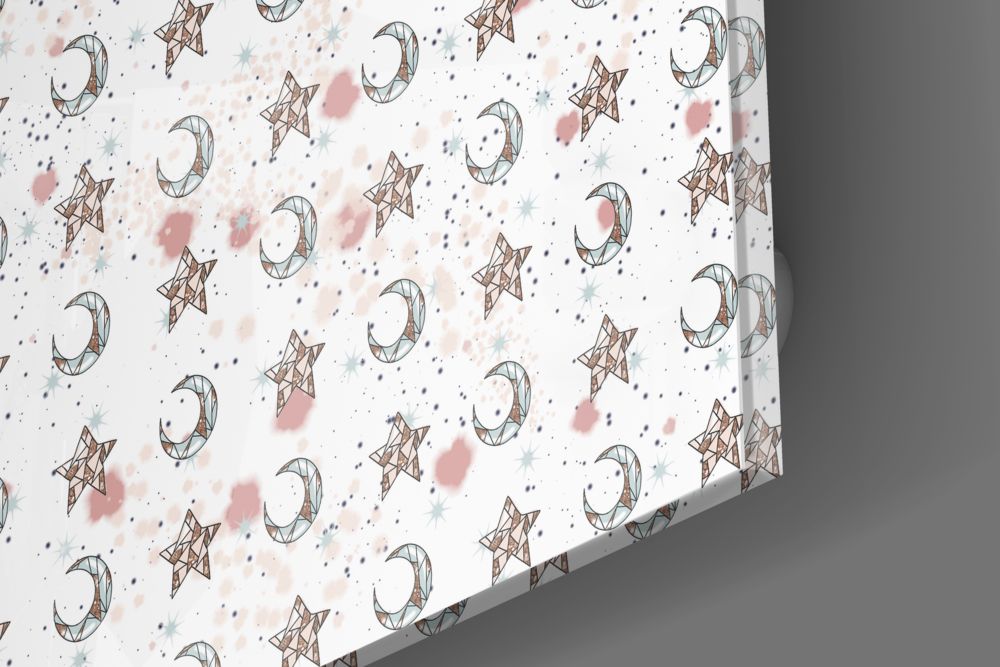 Close-up angled view of glass wall art showing repeating pattern of brown moons and stars with pink and blue watercolor splashes on white background.