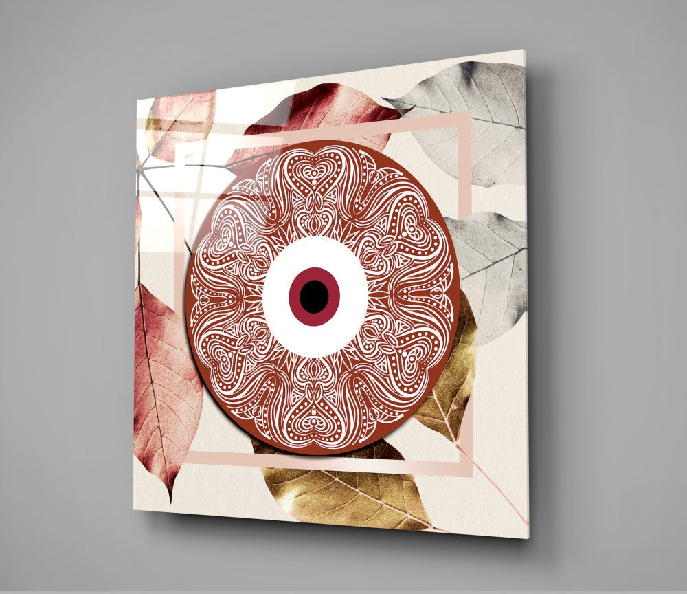 Square glass wall art displaying an ornate red and white mandala-style eye design surrounded by autumn leaves in cream, pink, and gold tones.