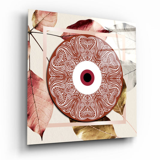 Red ornamental evil eye design on glass canvas with burgundy, gold, and cream autumn leaves against beige background, angled three-quarter view.