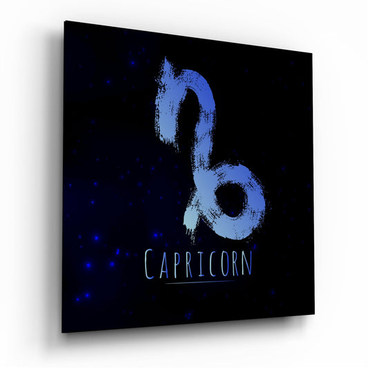 Angled perspective of glass wall art displaying blue brushstroke Capricorn symbol on black starry background with text label.