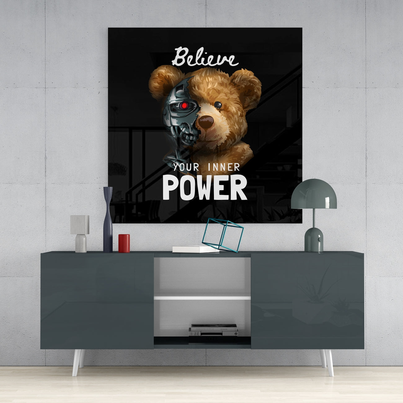 Black glass wall art featuring a teddy bear with a metallic robot half-face and red eye, displaying "Believe YOUR INNER POWER" text, mounted above a gray media console.
