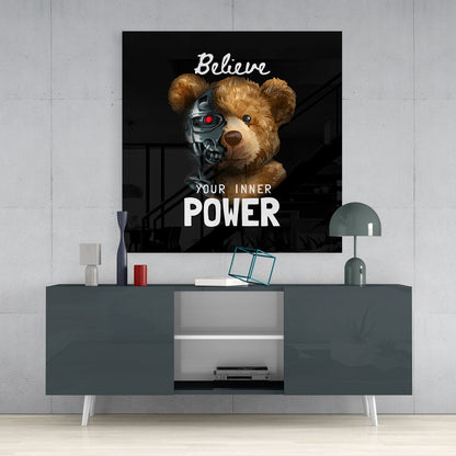 Black glass wall art featuring a teddy bear with a metallic robot half-face and red eye, displaying "Believe YOUR INNER POWER" text, mounted above a gray media console.