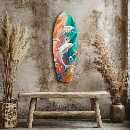 Colorful glass surfboard-shaped wall art depicting three leaping dolphins in coral, teal, and orange tones, displayed above a wooden bench against a textured beige wall.