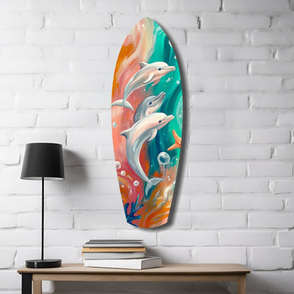 Colorful glass surfboard wall art featuring three dolphins against vibrant orange, teal, and coral gradient background, displayed on white brick wall.