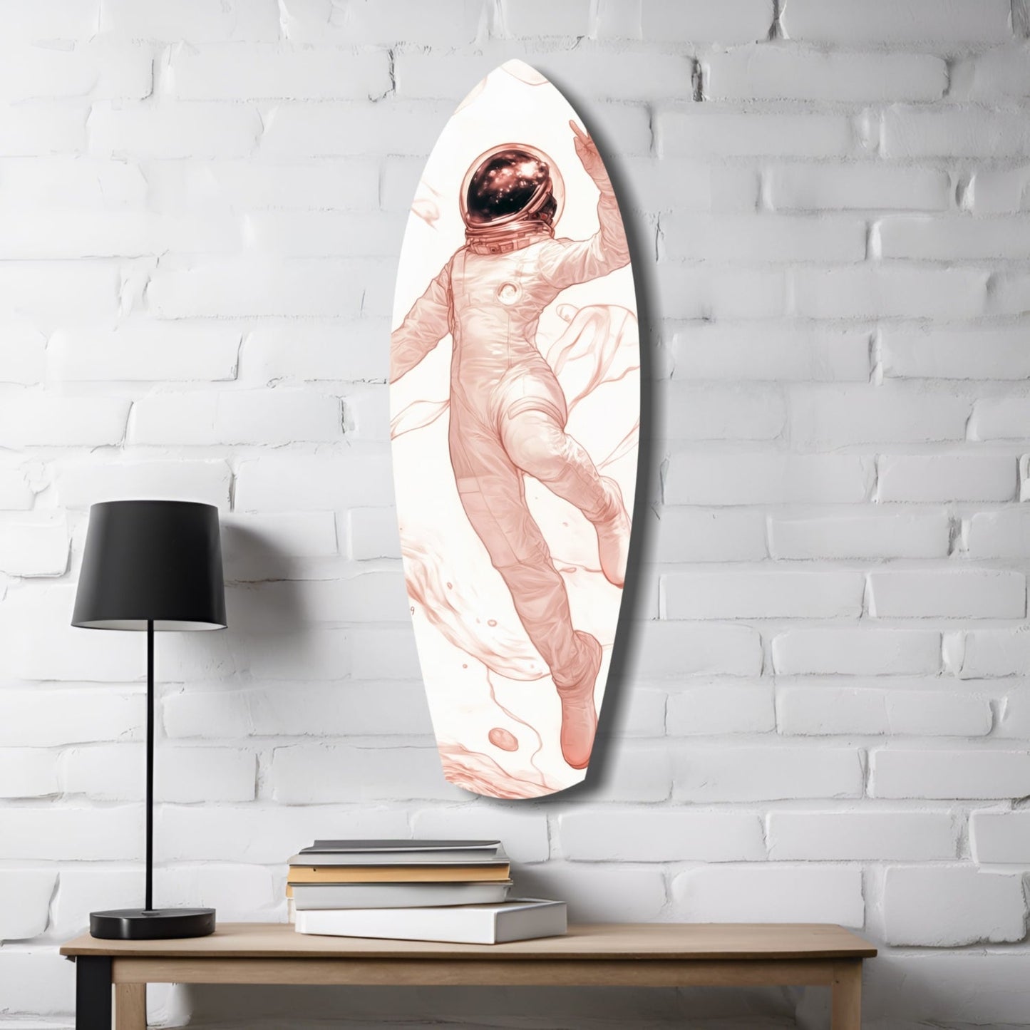 Oval glass wall art depicting a floating astronaut in rose tones against white brick, displayed above a wooden desk with lamp and books.