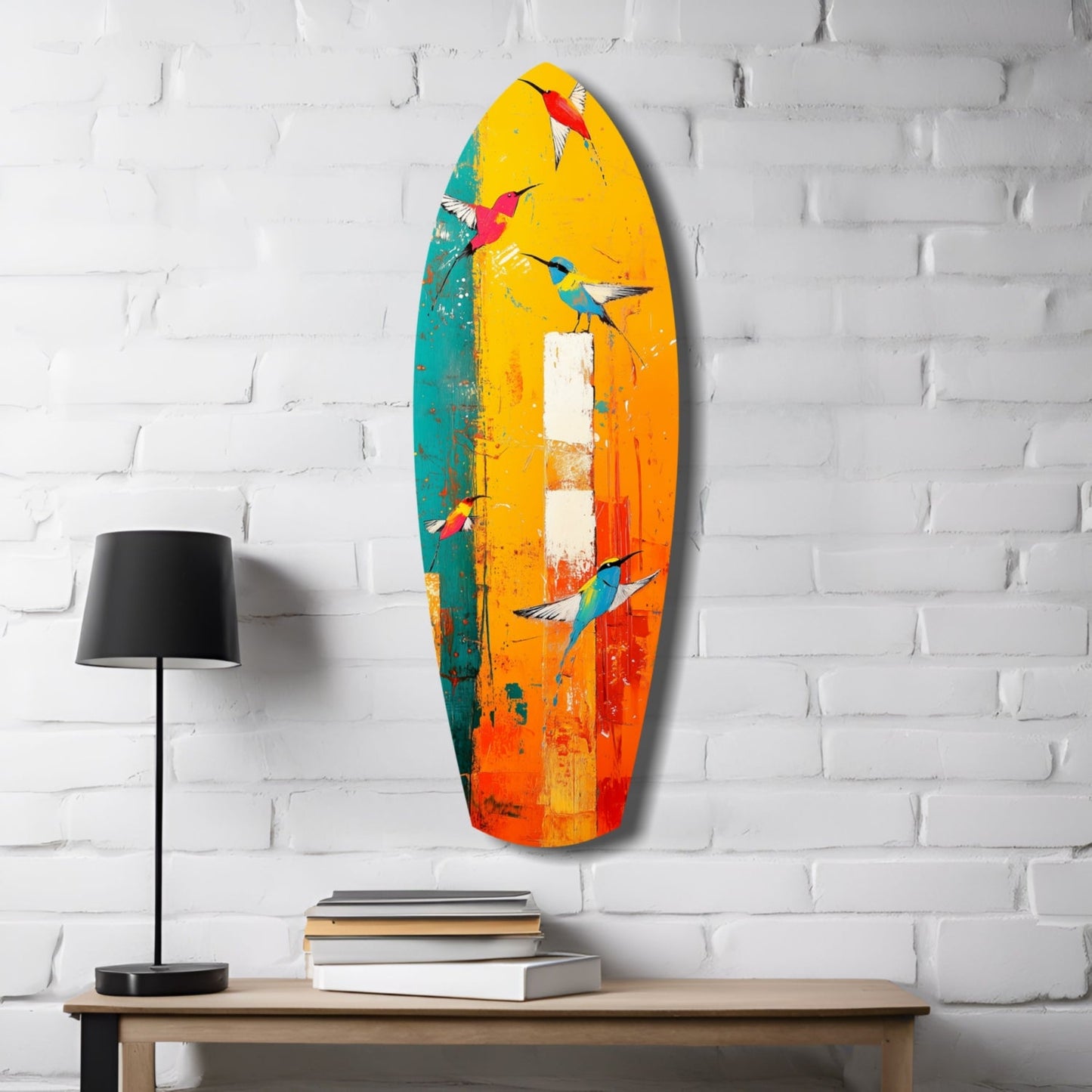 Colorful glass surfboard wall art featuring painted hummingbirds in yellow, orange, teal, and red tones, displayed above a wooden shelf with lamp and books.