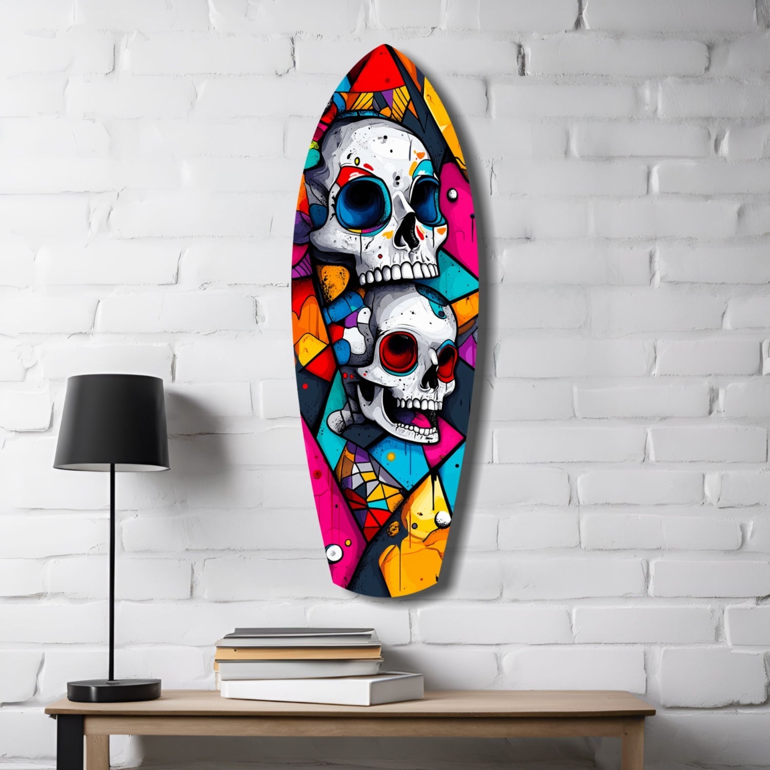 Colorful glass skull wall art mounted on white brick with two stacked skulls featuring bright geometric patterns in red, yellow, blue, and pink, displayed above a wooden table with lamp and books.