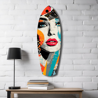 Colorful pop art glass wall hanging featuring a woman's face with red lips and blue eye, displayed on white brick wall above wooden desk with lamp and books.