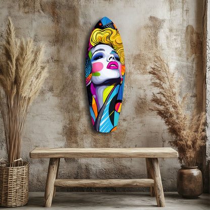 Colorful pop art glass wall art depicting a woman's face with blonde hair and bold makeup, displayed above a wooden bench in a rustic interior setting.