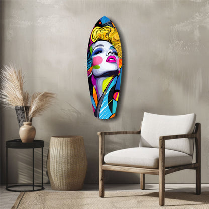 Colorful pop art glass wall sculpture of a woman's face with yellow hair and blue eyes displayed above a wooden chair in a minimalist interior.
