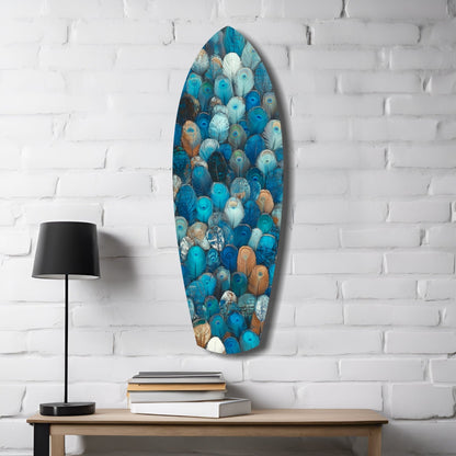 Feathers of the Haven Glass Wall Art displayed on white brick wall above wooden table with black lamp and stacked books, showing blue, teal, brown, and white feather pattern.