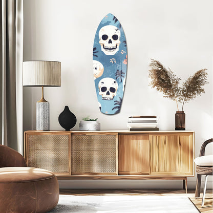 Surfboard-shaped glass wall art with two white skulls and tropical foliage on blue background, displayed above wooden mid-century dresser in modern living room.