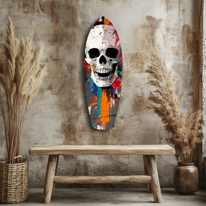 Colorful street art skull glass panel mounted on distressed wall above wooden bench, surrounded by dried pampas grass.