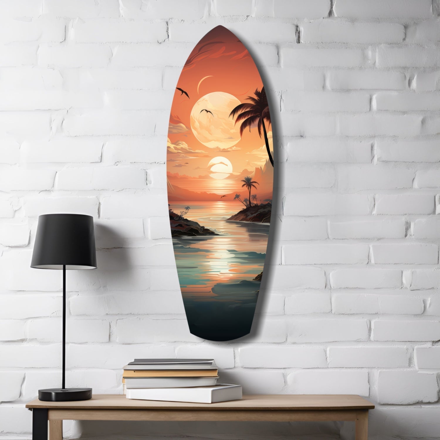 Surfboard-shaped glass wall art displaying a tropical sunset with palm trees, moon, and ocean, mounted on white brick above a wooden table with lamp and books.
