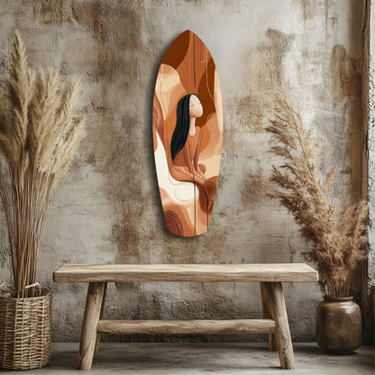 Feather-shaped glass wall art in warm terracotta and cream tones depicting a woman with dark hair, displayed above a wooden bench in a minimalist interior setting.