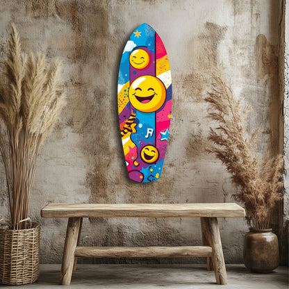 Colorful smiley face glass wall art mounted above wooden bench, featuring yellow emoji faces, blue pink and purple sections, against textured beige wall with dried grasses.