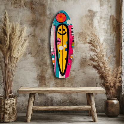 Colorful smiley surfboard glass wall art hanging above wooden bench, flanked by dried pampas grass in natural interior setting.