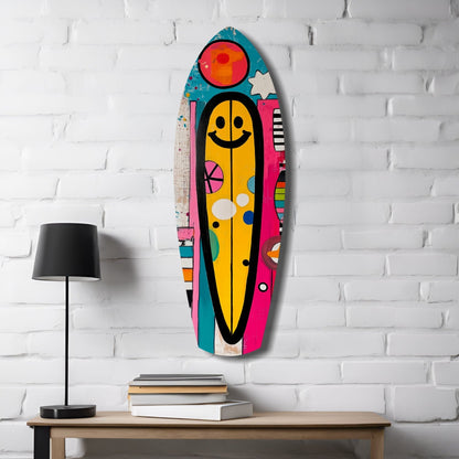 Colorful surfboard-shaped glass wall art with yellow smiley face and geometric patterns displayed on white brick wall above wooden table with lamp and books.