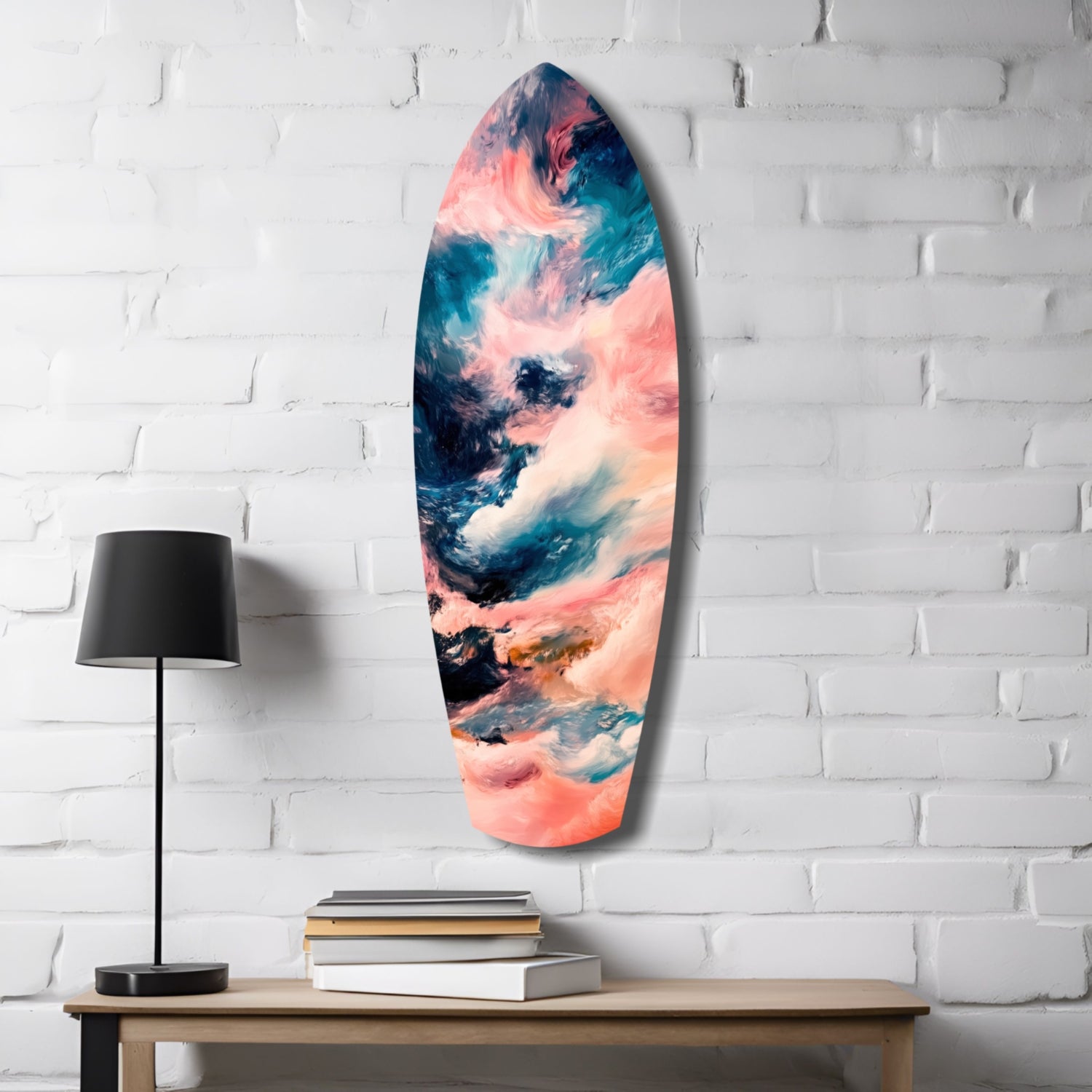 Surfboard-shaped glass wall art with coral, teal, and white abstract cloudy patterns displayed above a wooden desk with lamp and books.