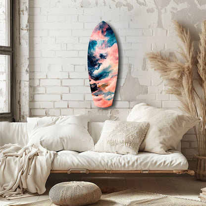 Surfboard-shaped glass art with pink, blue, and teal cloud patterns displayed on white brick wall above cream bedding.