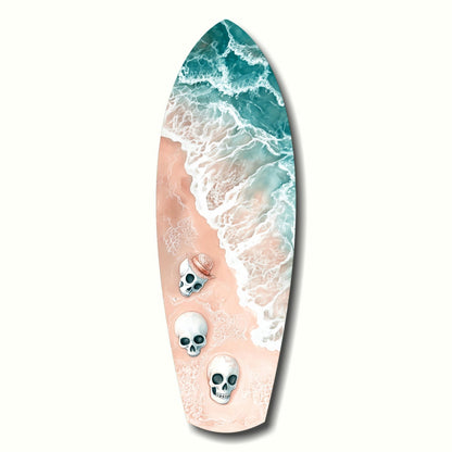 Surfboard-shaped glass art featuring aerial ocean waves in teal and white with sandy beach in peach tones and three skull decorations down the center.