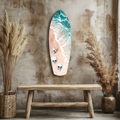 Surfboard-shaped wall art with turquoise ocean waves and three skull motifs on peach sand, displayed above wooden bench with dried grasses.