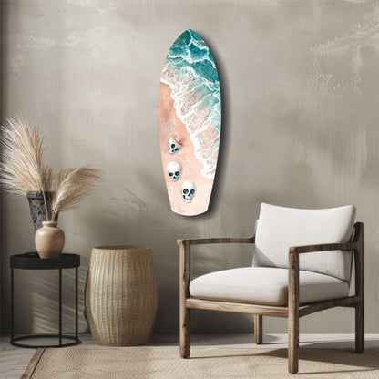 Surfboard-shaped wall art featuring ocean waves, sandy beach, and three skull designs mounted above a wooden chair in a coastal-styled room.