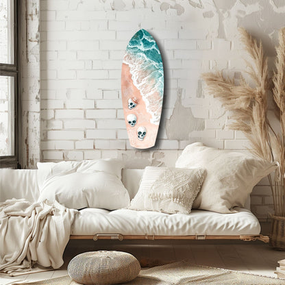 Surfboard-shaped wall art with turquoise ocean waves and coral sand beach featuring three skull designs, displayed above a cream bedding setup.