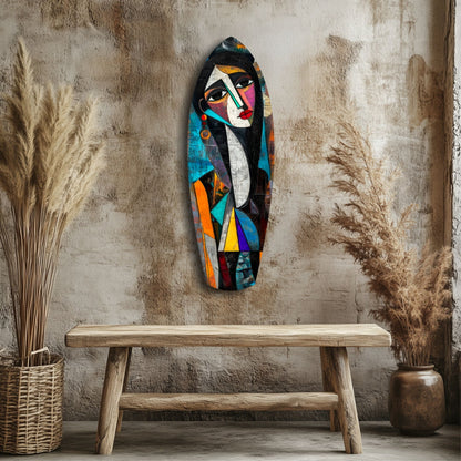 Colorful abstract glass wall art depicting a cubist face in blues, oranges, and blacks, displayed above a wooden bench in a styled room with dried grasses.