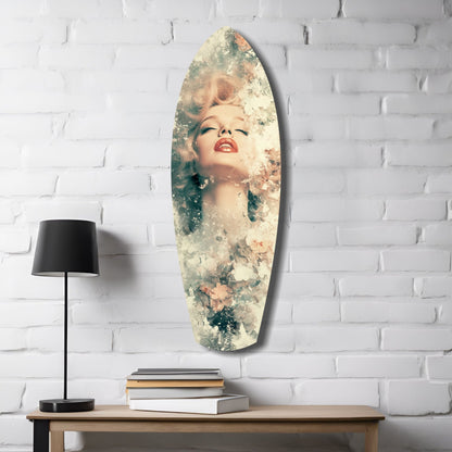 Oval floral glass wall art displaying a blonde woman's face with red lips, blended with soft green and cream botanical elements, mounted on white brick above wooden table with lamp and books.