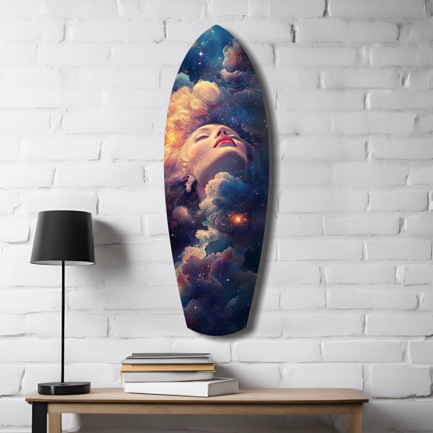 Celestial Dreamer glass wall art mounted on white brick above wooden table with black lamp and stacked books, featuring woman's face surrounded by cosmic clouds and stars.