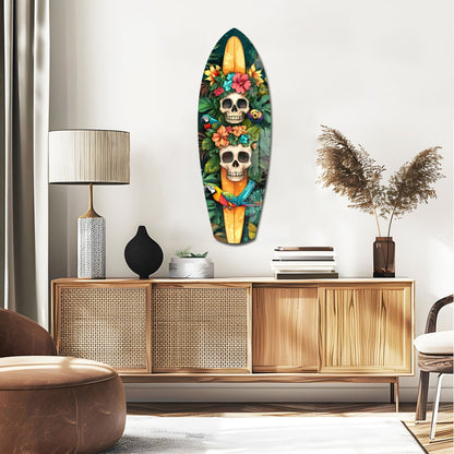 Decorative glass surfboard wall art featuring two skulls adorned with colorful flowers against dark green foliage, displayed above wooden mid-century dresser in modern living room setting.