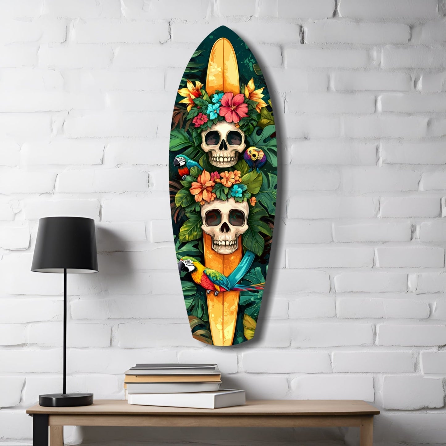 Surfboard-shaped glass art hanging on white brick wall above wooden desk with lamp and books, featuring two skulls surrounded by colorful flowers and a parrot.