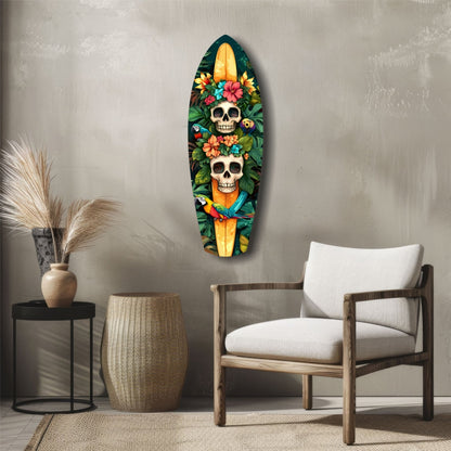 Surfboard-shaped glass wall art with two colorful skulls surrounded by tropical flowers and parrots, displayed above a wooden chair in a minimalist interior.