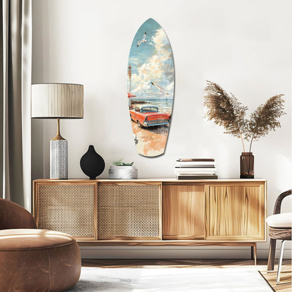 Surfboard-shaped glass wall art depicting a vintage red car on a beach with blue sky and clouds, displayed above a wooden credenza in a modern interior.