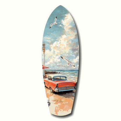 Surfboard-shaped glass art depicting a red vintage 1950s car parked on a beach with a lighthouse, seagulls, and cloudy sky.
