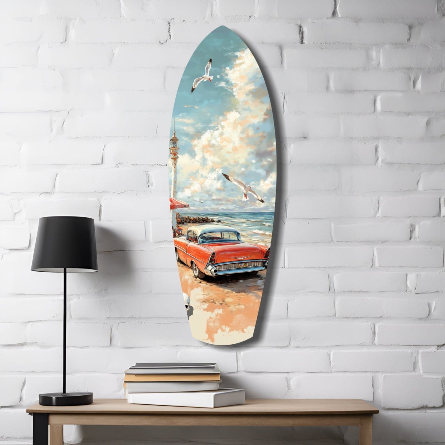 Surfboard-shaped glass wall art hanging on white brick displays a vintage red car on a beach with lighthouse, sailboats, and blue sky scene.
