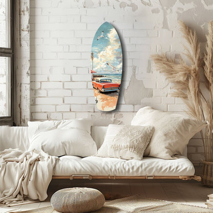 Surfboard-shaped glass wall art displaying a vintage red car on a beach with sailboats and blue sky, hanging on white brick above a cream bedframe.