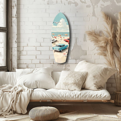 Surfboard-shaped glass wall art depicting a vintage 1950s beach scene with turquoise car, umbrellas, and ocean, displayed above a cream linen sofa.