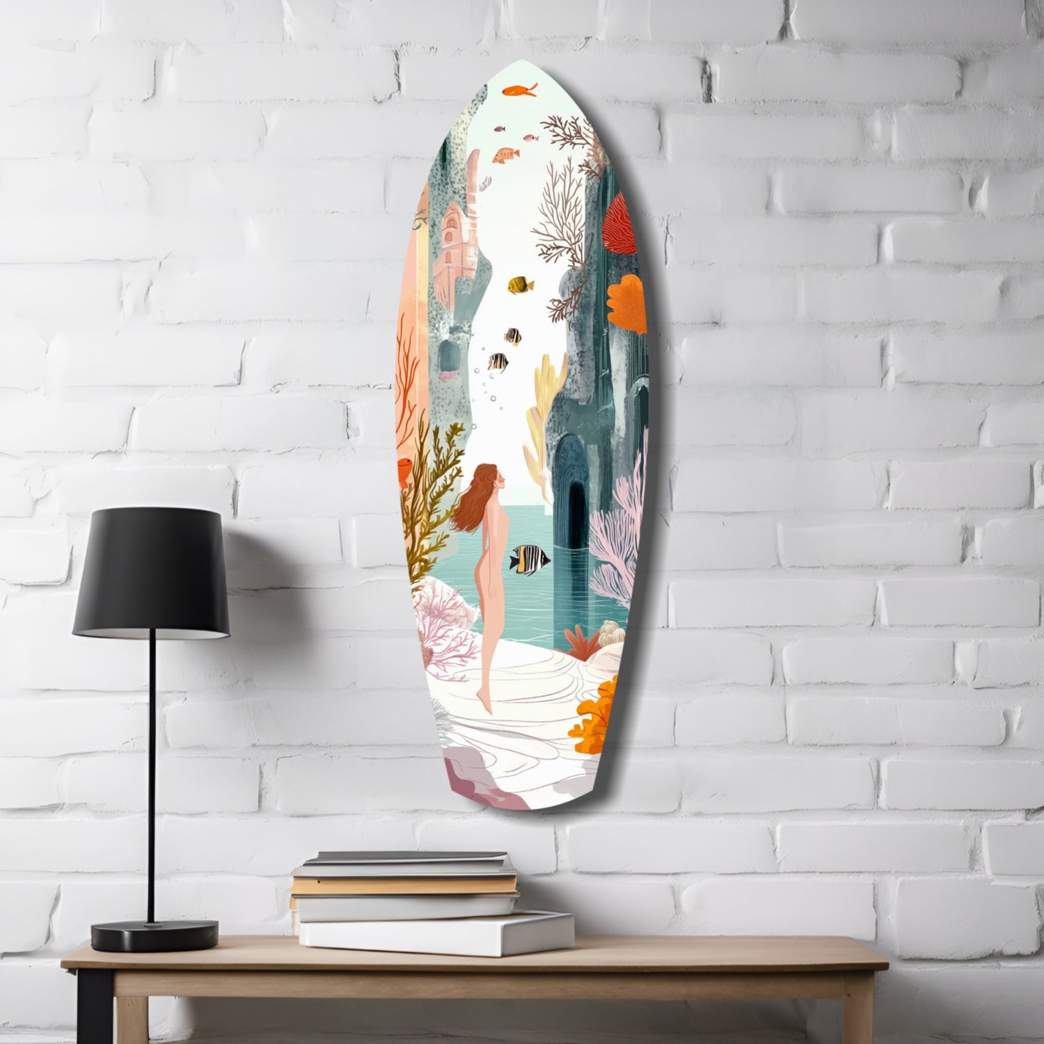 Oval glass wall art depicting an underwater scene with a swimmer, colorful fish, coral, and seaweed in muted tones, displayed on white brick above a wooden table with lamp and books.