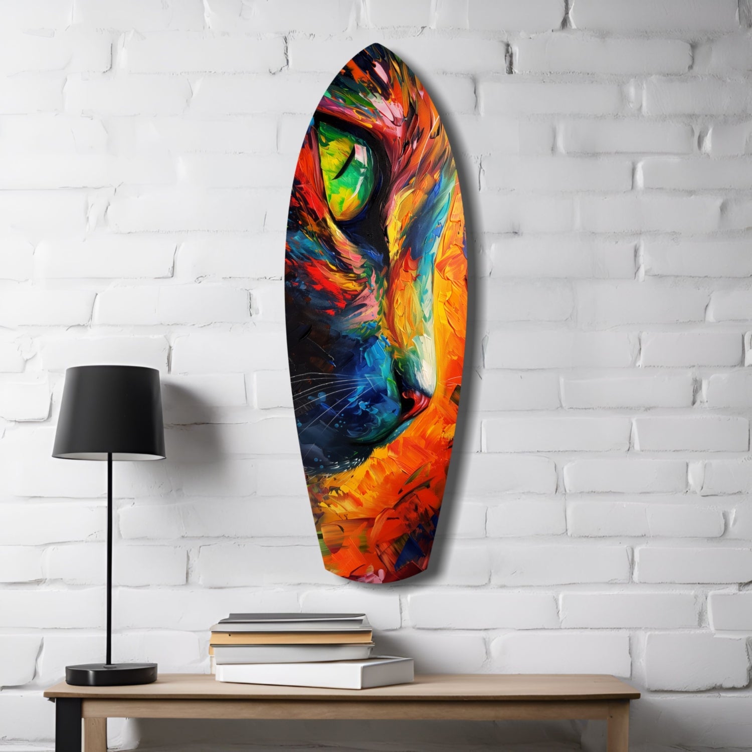 Colorful glass cat wall art mounted on white brick, displayed above wooden desk with black lamp and stacked books.