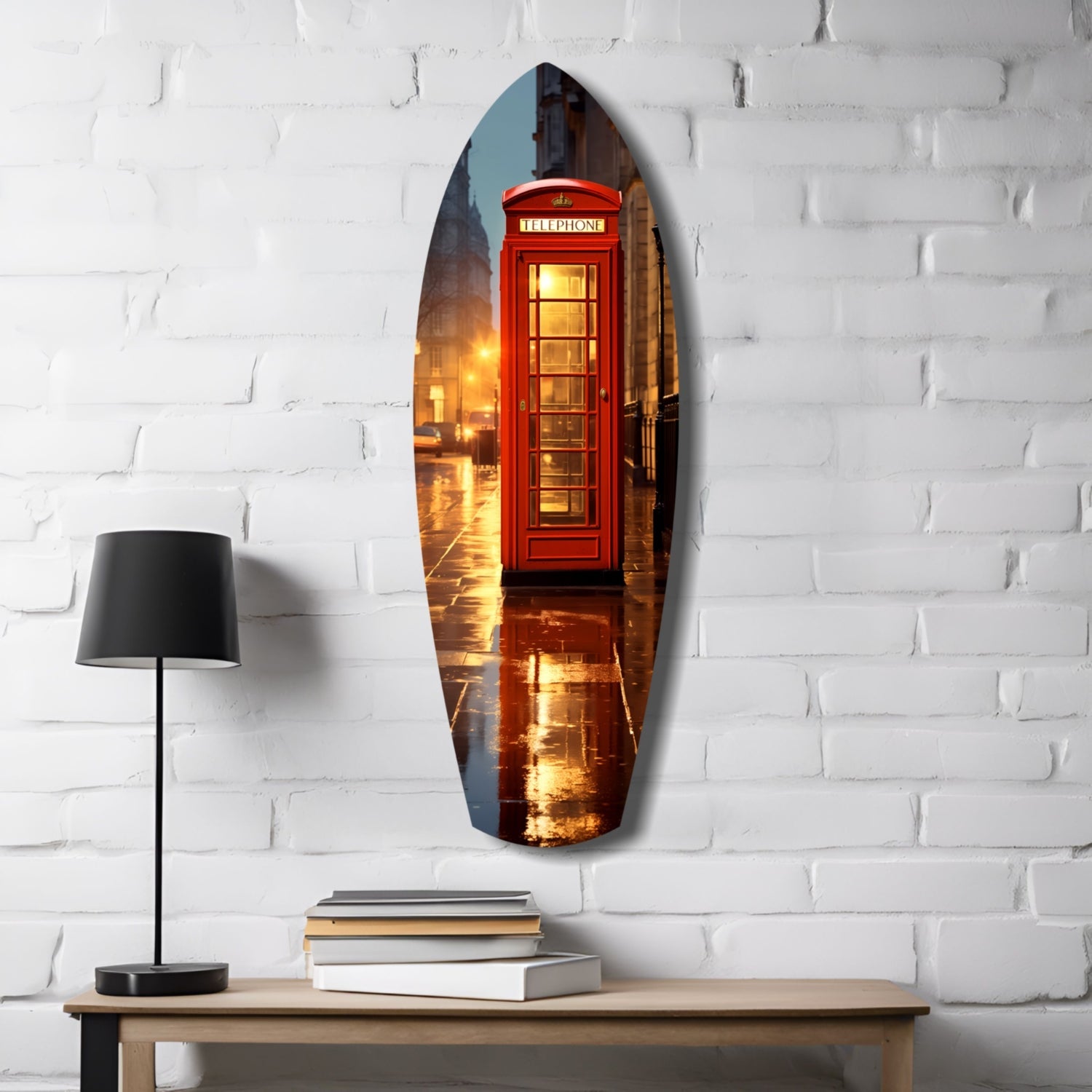 Oval glass wall art depicting a glowing red British telephone booth on a wet London street, hung on white brick with a lamp and books below.