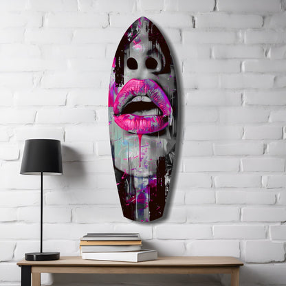 Oval glass wall art with vibrant pink lips and dark eyes mounted above wooden desk with lamp and stacked books against white brick.