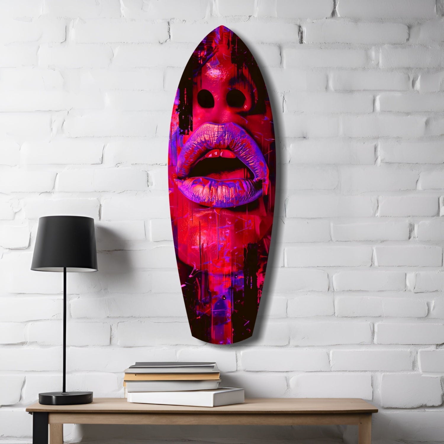 Neon pink and purple lips glass wall art mounted on white brick above wooden desk with lamp and books.